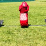 A front view of a five-man American football blocking sled with red, player-shaped padding on a green field.
