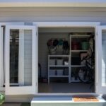 A contemporary shed with gray siding and large glass swing-out doors, situated in the center of the yard.