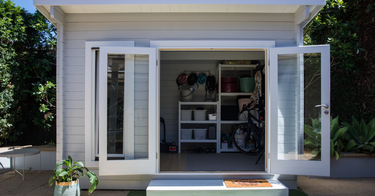 A contemporary shed with gray siding and large glass swing-out doors, situated in the center of the yard.