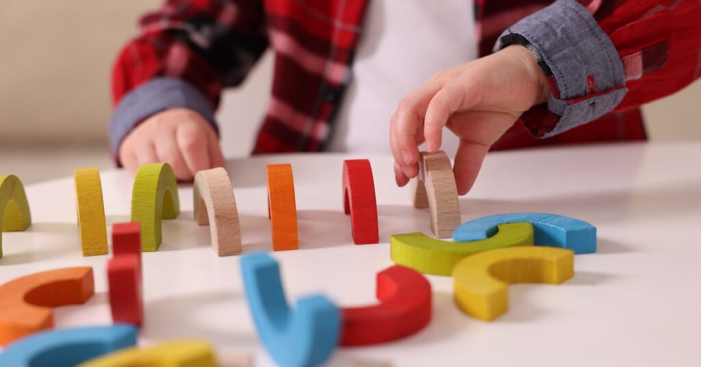 A close-up of a toddler's hands as they play with and organize colorful wooden play toys on a white table.