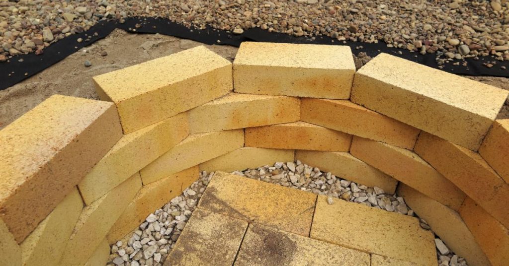 A DIY fire pit uses bricks stacked on top of each other, creating a circle. Bricks are at the bottom, creating a flat surface.