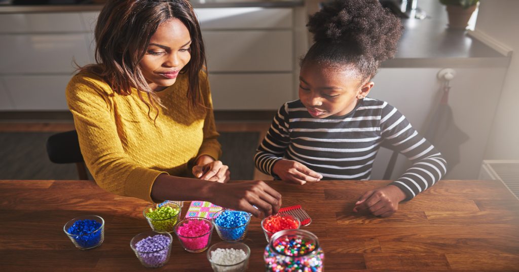 A mother and daughter sitting at a table together to work on creating art using colorful, iron-fusible beads.