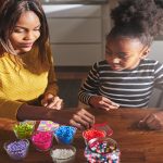 A mother and daughter sitting at a table together to work on creating art using colorful, iron-fusible beads.
