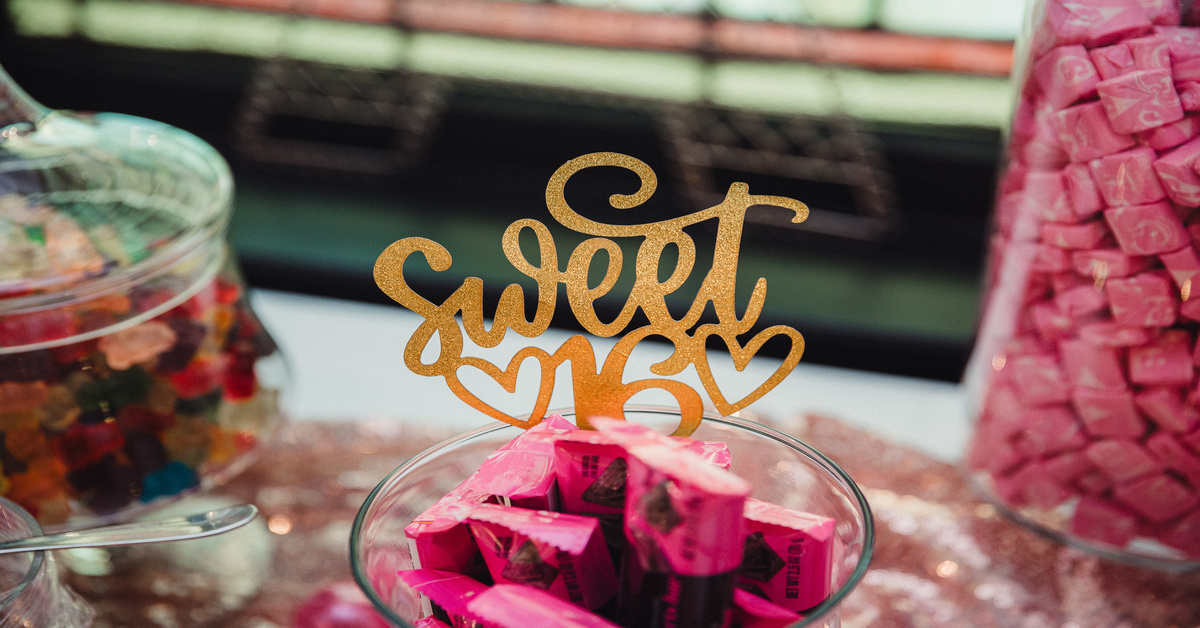 Three glass containers filled with candies, including gummy bears and Starbursts, with a "Sweet 16" topper in the center jar.