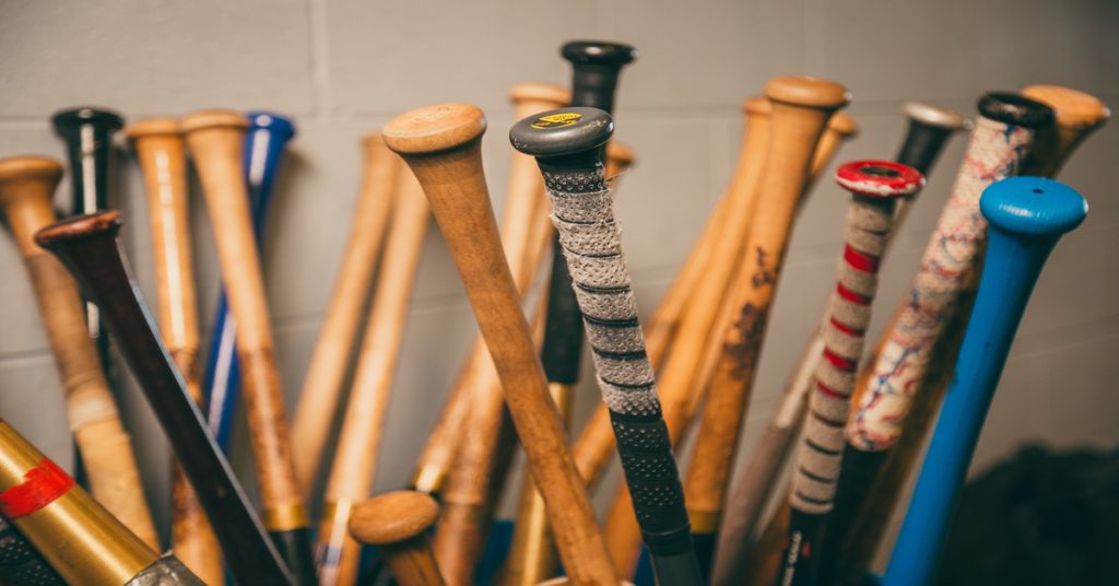 Numerous baseball bats are upside down against a white wall. Some bats are made of wood, while others are made of aluminum.