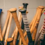 Numerous baseball bats are upside down against a white wall. Some bats are made of wood, while others are made of aluminum.