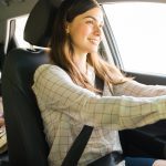 A woman smiles as she drives a vehicle with two children in the back. Both kids look at a storybook.