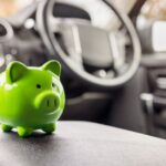 A close-up of a small, neon-green piggy bank on the center console inside a car, with the steering wheel in the background.