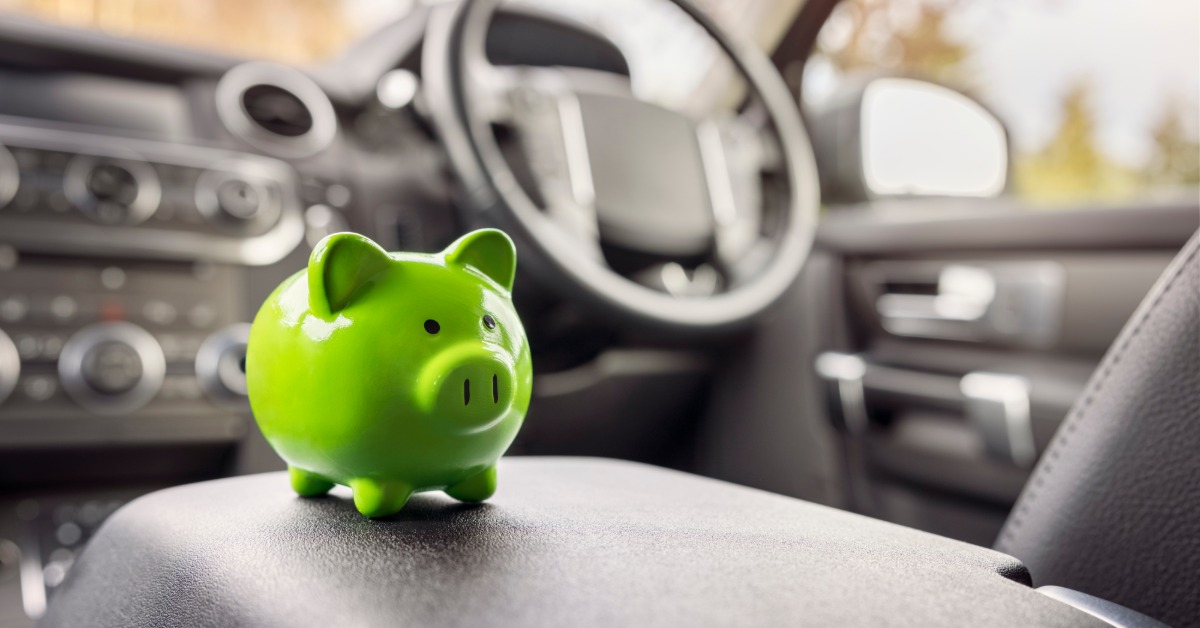 A close-up of a small, neon-green piggy bank on the center console inside a car, with the steering wheel in the background.
