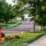 A residential neighborhood with the initial stages of fiber network install, including small yellow flags and an orange cone.