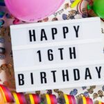 Home 8 An LED light board with bold letters that say "happy 16th birthday." There are balloons and confetti surrounding the board.